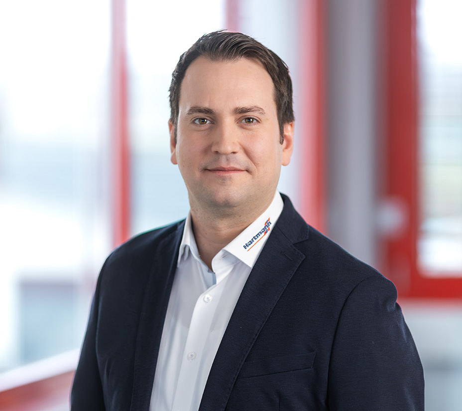 Mitarbeiter von Hartmann im Business-Outfit vor rotem Fensterrahmen.